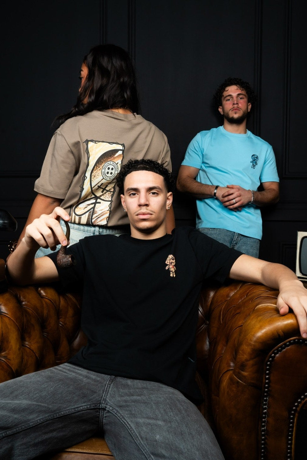Three individuals in a casual setting with one sitting on a leather couch.