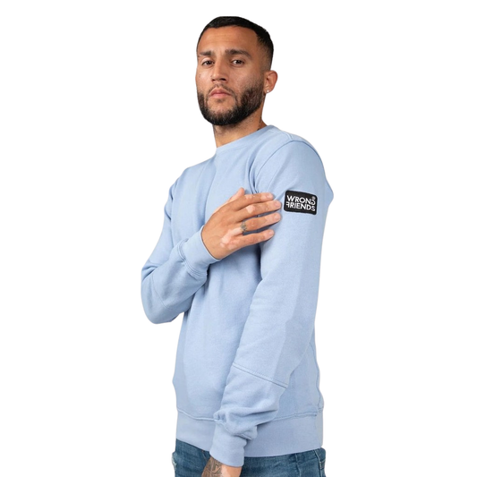 Model wearing the light blue Wrong Friends Leon crewneck, with branded sleeve patch.