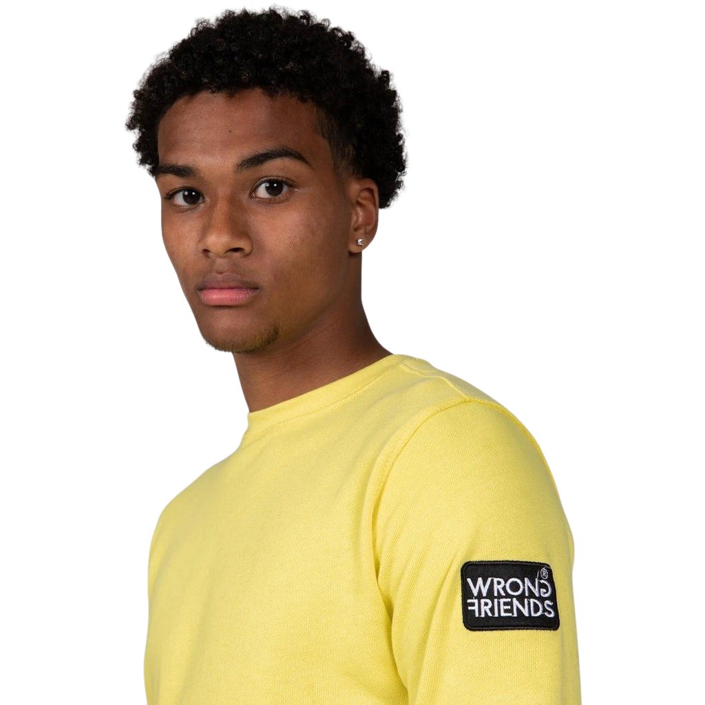 Model wearing the yellow Wrong Friends Leon crewneck, with the branded sleeve patch